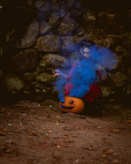 woman witch in red dress in a medieval castle with smoke blue pumpkin. The medieval queen.  Evil witch