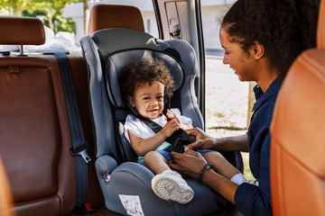 Young female fastening her smiling son into a baby seat