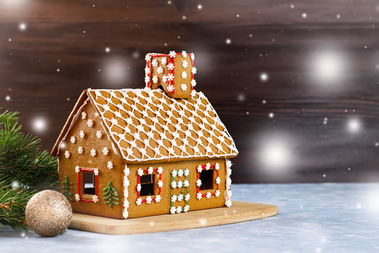 Decorated gingerbread house closeup with pine decorations and golden balls in background.