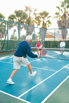 Group of active seniors, men and women, playing platform tennis on tennis court.