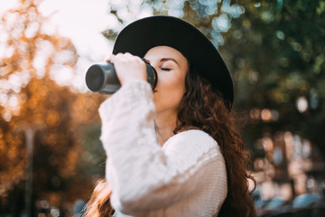 Stylish young woman walking in autumn city with thermo mug