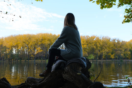 Autumn girl sitting backwards on lake and forest 
