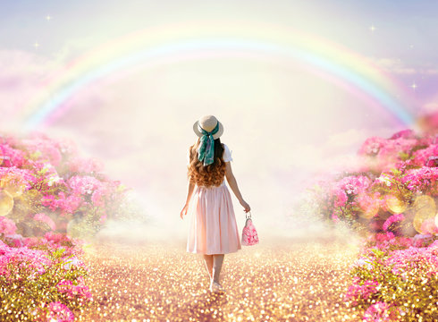 Young Lady Woman In Romantic Pink Dress, Retro Hat, Bag Walking Along Rose Garden Path Leading To Fabulous Rainbow Unicorn House, Flecks Of Sunlight On Road. Tranquil Fantasy Scene, Fairytale Hills.