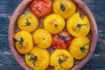 Baked red and yellow tomato. Tomatoes in a baking dish on a wooden table. A healthy and delicious vegetarian dish. Closeup, top view