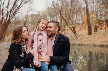 Happy family. The father and mother embracing their daughter relaxing outdoors in autumn park