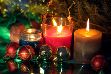 Festive christmas burning candles ubder the tree with gift box and baubles