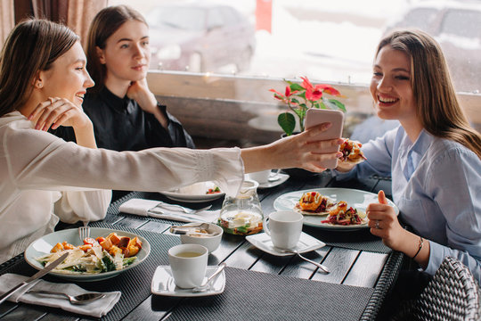 Three girlfriends having lunch together at cafe . One o them showing something on her phone for other one