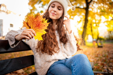 Naklejka na ściany i meble Outdoor lifestyle portrait of young woman with warm hat holding colorful autumn leaves and smiling