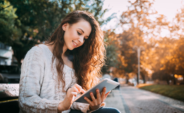Joyful girl in autumn scenery using digital tablet outdoors browsing internet