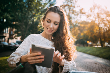 Joyful girl in autumn scenery using digital tablet outdoors browsing internet