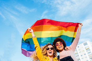 Two women friends hanging out in the city waving LGBT with pride flag
