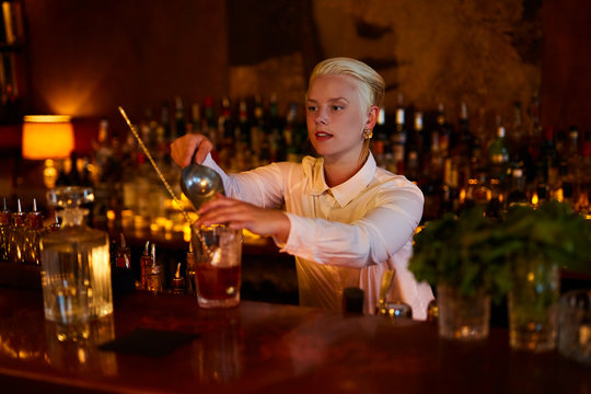 A bartender loading ice cubes into the glass.