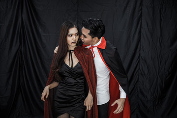 Asian young couple in costume witch and dracula on black cloth background.