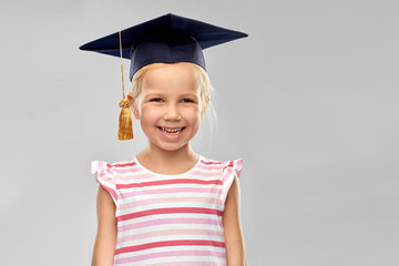 school, education and learning concept - happy little girl in bachelor hat or mortarboard over grey background