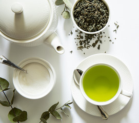 Green tea - tea leaves, teacup, teapot, sugar bowl on a white background, top view, close-up.