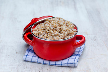 Red pan with boiled wheat porridge . Closeup