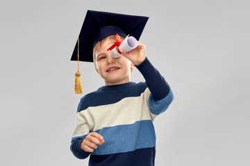 school, education and learning concept - happy little boy in bachelor hat or mortarboard looking...