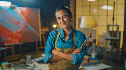 Portrait of Talented Young Female Artist Dirty with Paint, Wearing Apron, Crosses Arms while...