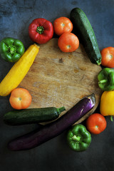 Colorful fresh mixed vegetables over black background with wooden cutting board