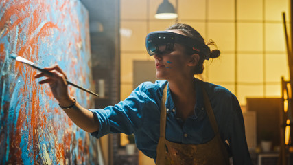 Talented Female Artist Wearing Augmented Reality Headset Working on Abstract Painting, Uses Paint Brush To Create New Concept Art Using Virtual Reality Interface. High tech Creative Modern Studio - obrazy, fototapety, plakaty