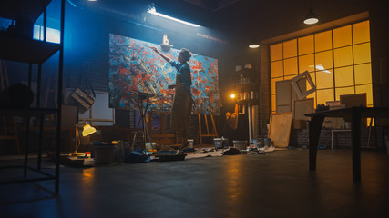 Talented Female Artist Walks to a Canvas and Starts Working on a Modern Abstract Oil Painting Using Paintbrush. In the Dark Creative Studio Large Picture Stands on Easel Illuminated, Tools Everywhere