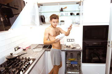 young man is cleaning the kitchen and takes out the dishes from the dishwasher.