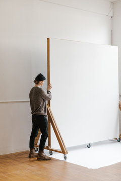 young man moving a rolling backdrop wall in photo studio