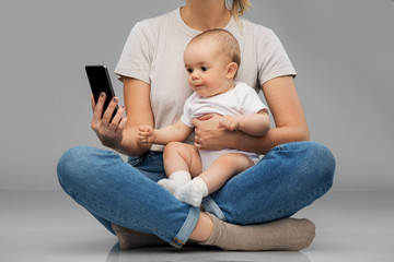 family, technology and motherhood concept - mother and baby looking at smartphone