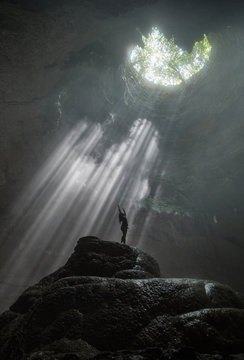 Girl stands under the rays of light in a deep cave Jomblang Cave. Java, Indonesia