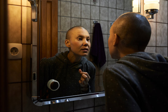 Hairless woman looking mirror.