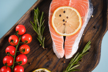Raw, fresh salmon steak on a wooden board with lemon, rosemary and cherry tomatoes. Raw salmon, red fish. Cooking salmon, seafood. Healthy eating concept. Salmon and spices