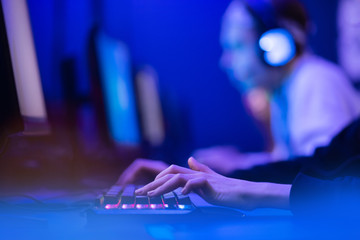 Professional online gamer hand fingers mechanical keyboard in neon color blur background. Soft focus, back view © Parilov