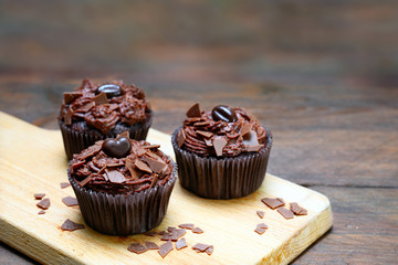 chocolate cupcakes with cocoa butter cream on a cutting board and a dark wooden table, copy space