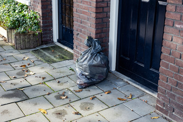 Garbage bag near a front door in a neighbourhood, ready for pick up