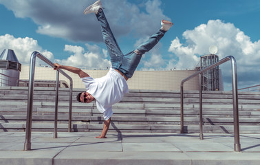 Male athlete, standing on one arm, summer city, hip hop style, break dancer. Building staircase background. Active youth lifestyle, modern fashionable, street dancer. Happy smiling fitness movement.