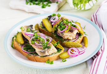 Traditional Dutch sandwich with herring and pickles cucumbers on white table. Smorrebrod.