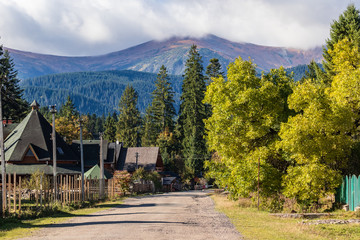 Deserted road in a small village at the foot of the mountains.  The tops of high mountains are hidden by clouds.  Autumn landscape. Panoramic view.