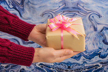 Woman holds christmas gift in her hands. Blue decorative background.