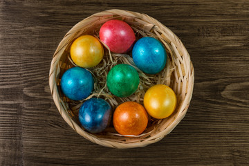 Colored Easter eggs in a basket on rustic wooden table.