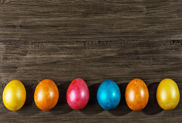 Colored Easter eggs in a basket on rustic wooden table.