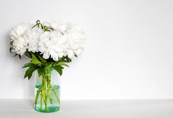 Bouquet of white peonies in a glass vase on a white wall background