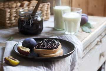Bread toast with plum jam, served with milk and plums on a wooden background. Rustic style.