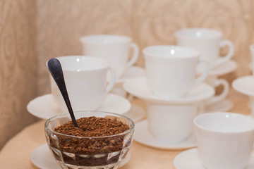 Instant coffee in a glass bowl on a background of white coffee cups