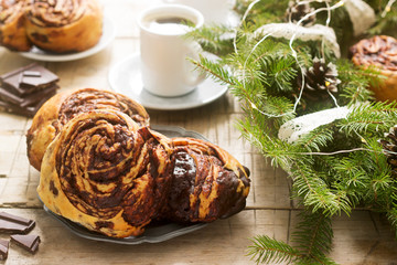 Snail chocolate muffins served with coffee on the background of a wreath of fir branches and cones. Rustic style.