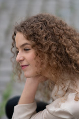 Fototapeta premium Profile view of young woman with curly hair resting her head on her hand