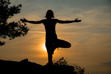 Fototapeta premium Young woman exercising yoga at dawn against sun, outdoor peace