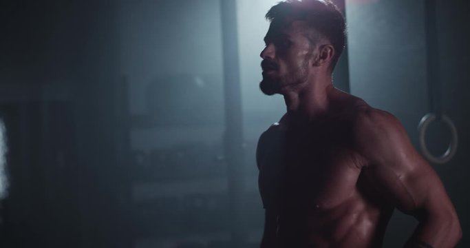 Charismatic guy with strong body stretching head and body before starting his workout in a dark cross fitness class he have a naked body