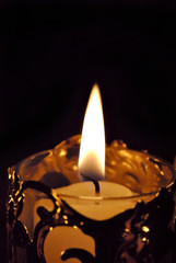 A single white votive candle in a golden holder.