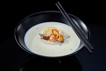Balinese cream soup with seafood in a black plate on a dark background