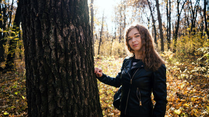 Beautiful woman looking out from behind tree. Pretty calm woman touching tree and looking at camera in quiet forest